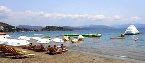 Una playa con tumbonas y sombrillas, un mar tranquilo y una cadena montañosa distante.