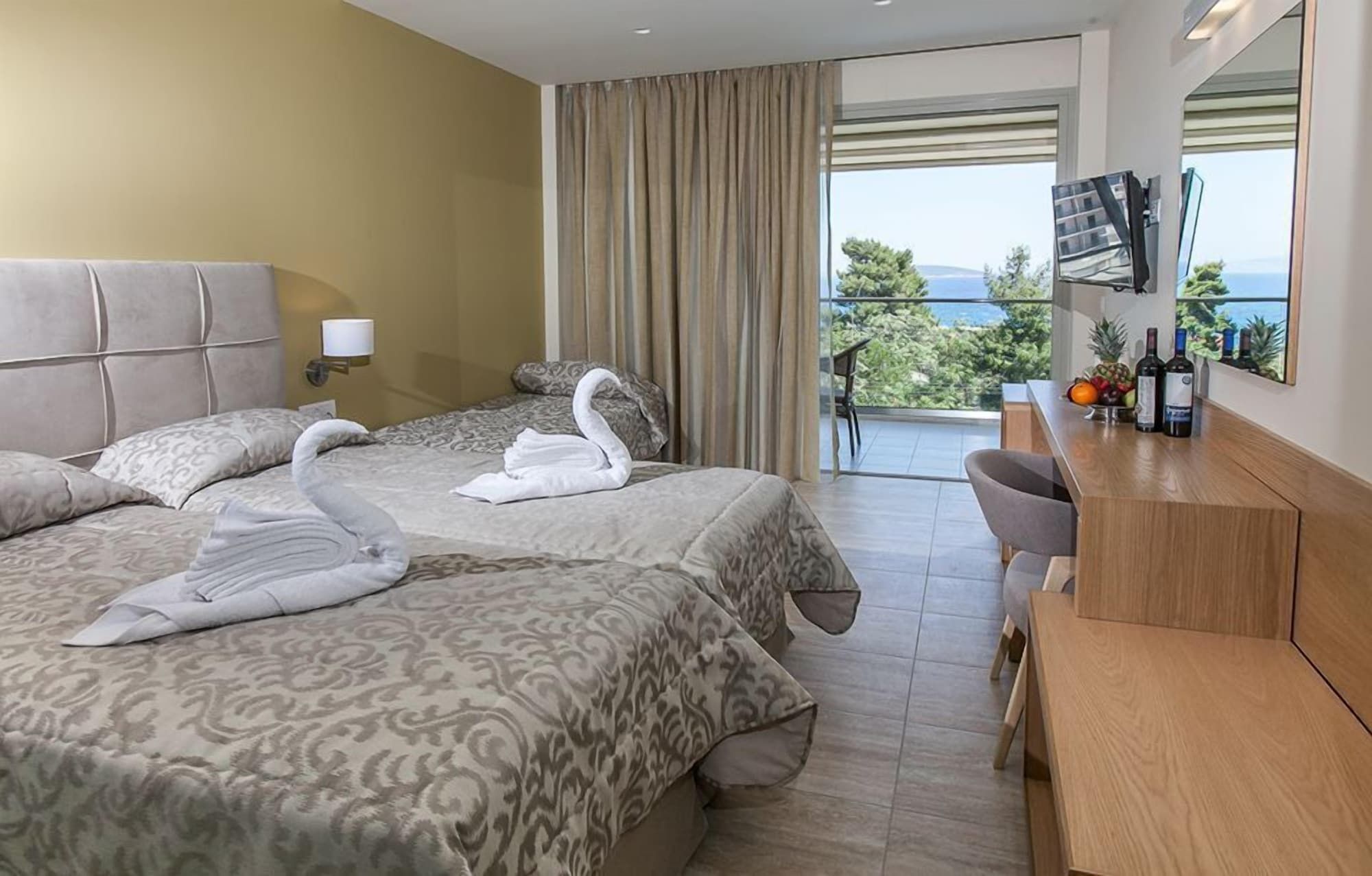 A hotel room with two beds, a desk with a chair, a TV, and a balcony with a view.