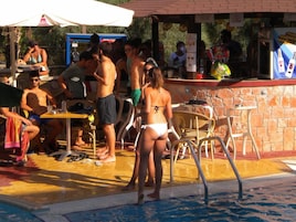 Zona junto a la piscina con bar y mesas.