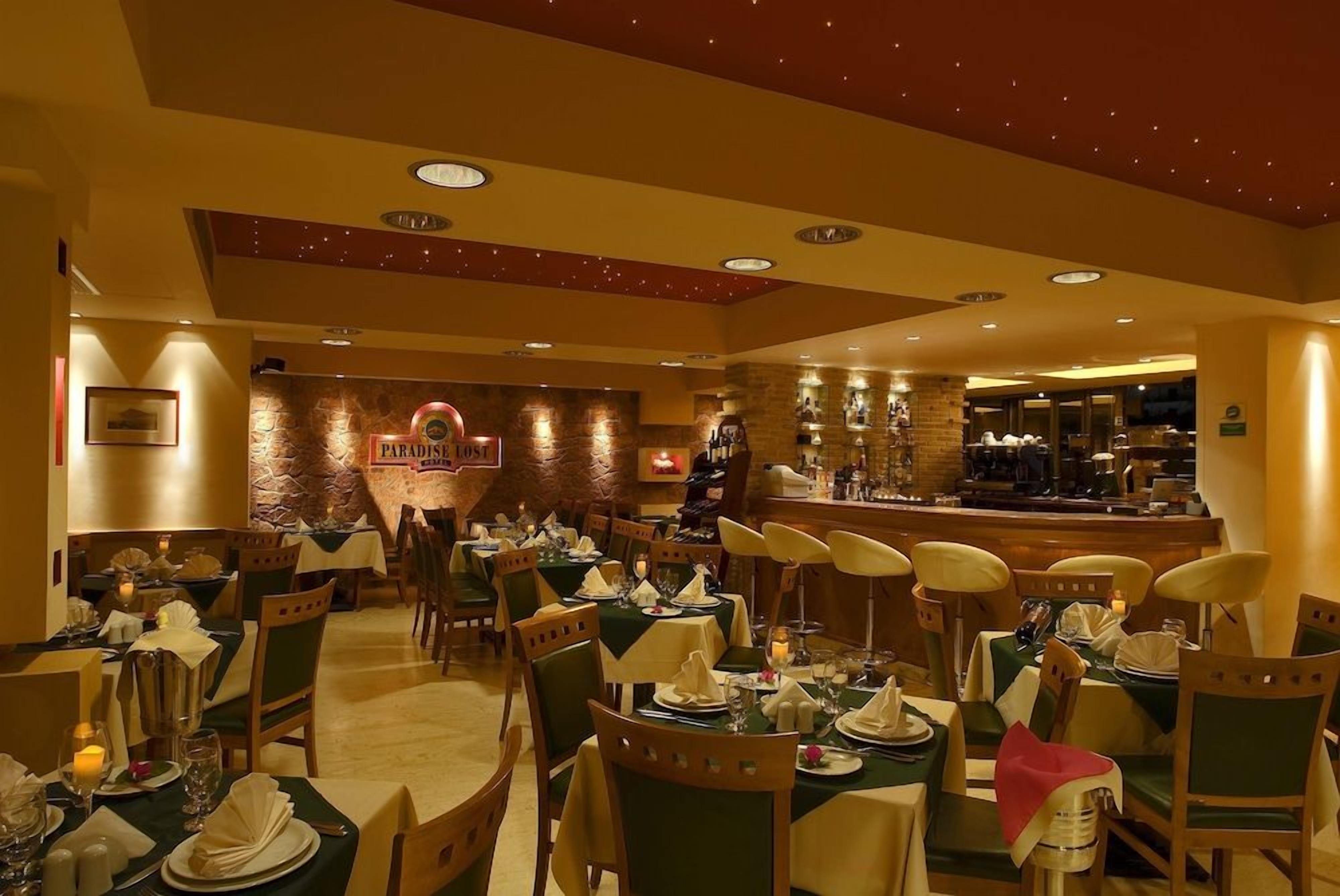A restaurant with multiple tables set for dining, a bar area, and a stone wall with a sign.