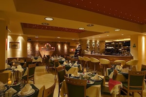 Un restaurante con varias mesas dispuestas para comer, una zona de bar y una pared de piedra con un letrero.