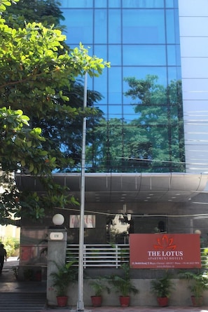 A modern building with a glass facade, a sign for The Lotus Apartment Hotels, and potted plants at the entrance. - The Lotus Service Apartments (Chennai)