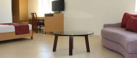 A hotel room with a bed, a sofa, a small table, a TV, and a desk.