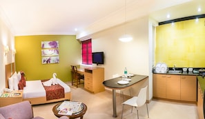 A hotel room with a bed, a desk, a dining table, and a kitchenette. - The Lotus Service Apartments (Chennai)