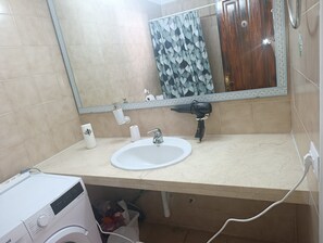 Un bagno con lavandino bianco, uno specchio, un erogatore di asciugamani e un asciugacapelli.