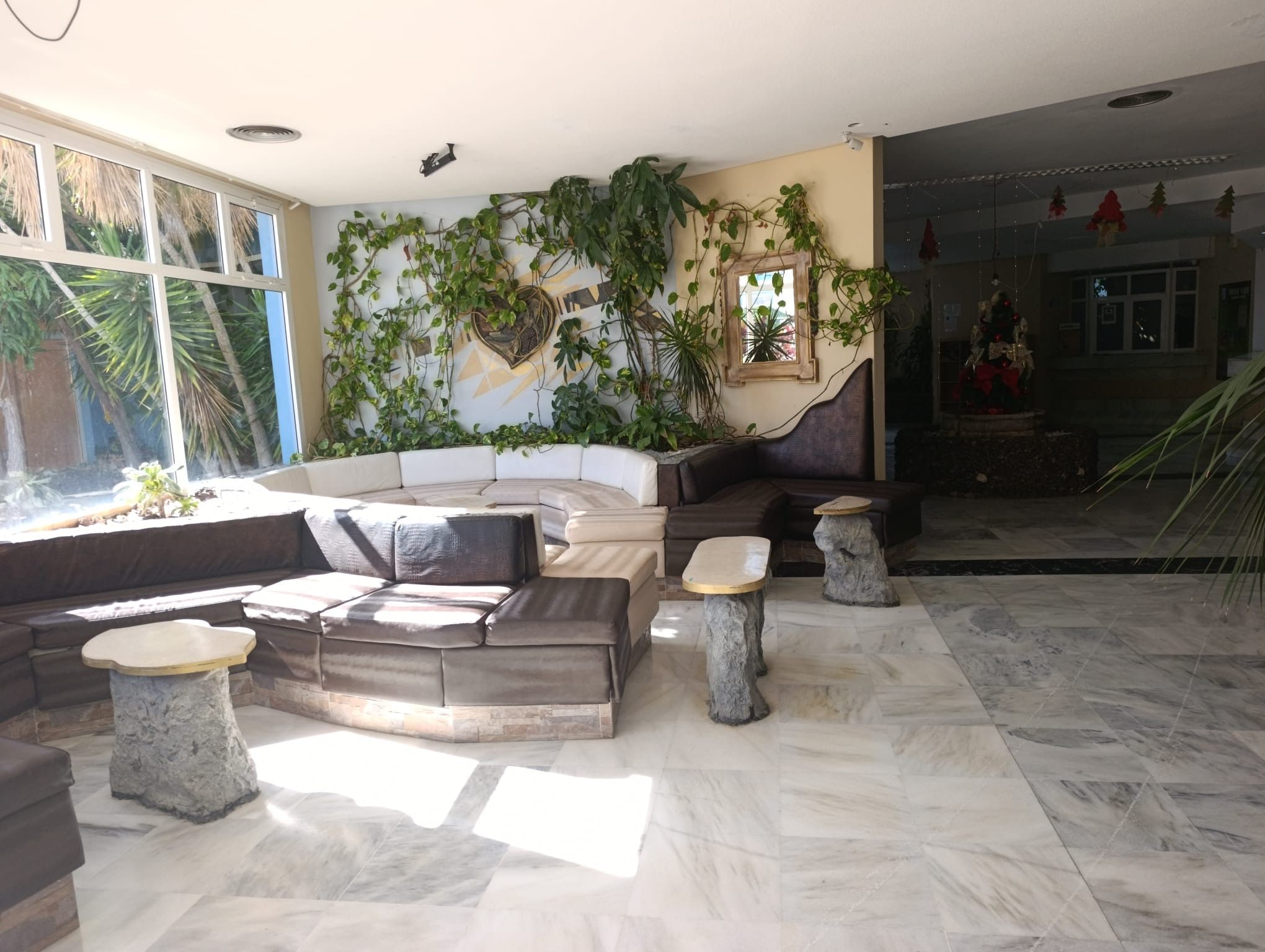 Una sala de estar moderna con un sofá modular, mesas auxiliares de piedra y un ventanal con vistas a palmeras.