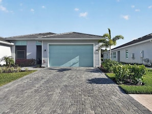 Ein eingeschossiges Haus mit Garage, befestigter Auffahrt und einem kleinen Garten mit verschiedenen Pflanzen.