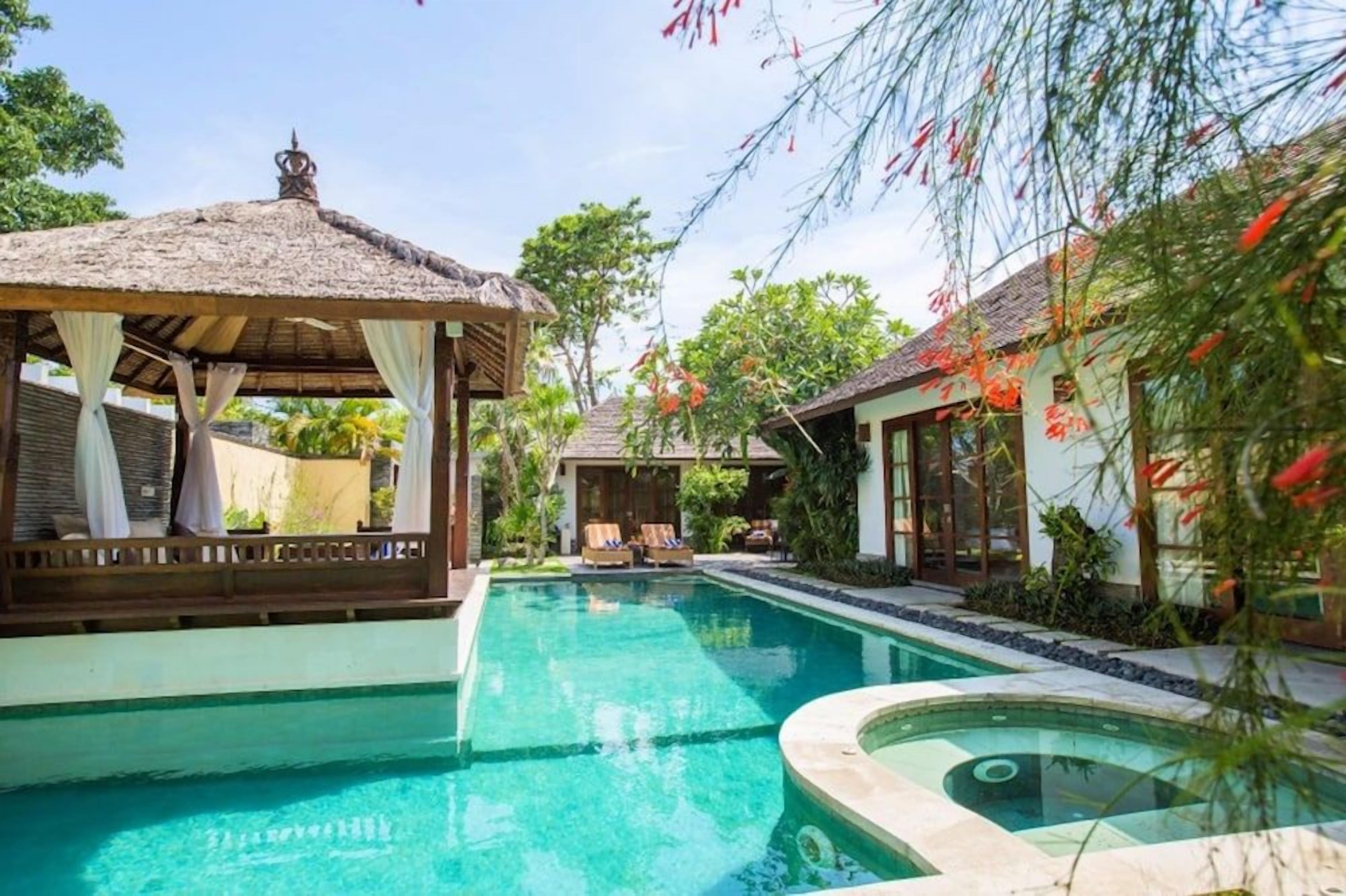 A swimming pool with a thatched-roof structure and lounge chairs.