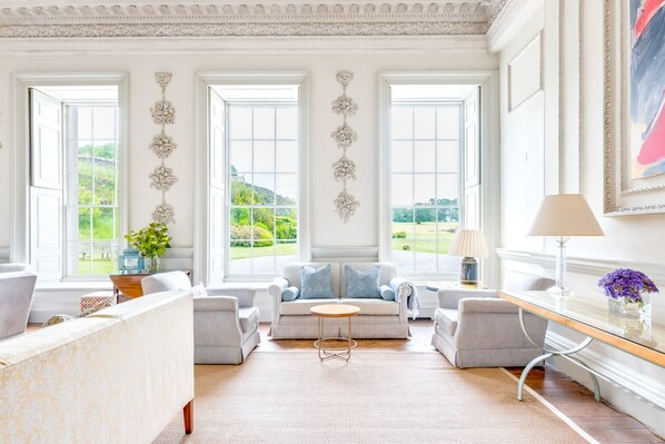 A spacious living room with a large window, a sofa set, a coffee table, and a lamp.