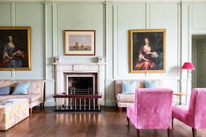 A room with a fireplace, two sofas, a table, and three paintings.