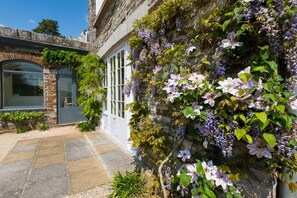 A stone building with a large window and a door, surrounded by lush greenery and flowering vines. - Lostwithiel Manor - Nine Bedroom Villa, Sleeps 18 (Boconnoc)