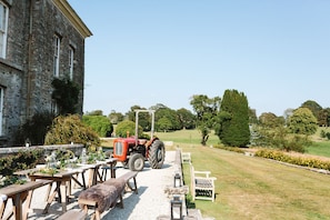 A stone building with outdoor seating and a red tractor in a landscaped garden.