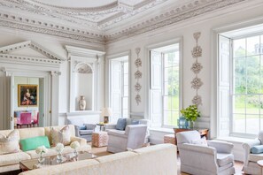 A spacious room with a high ceiling, ornate moldings, and large windows offering a view of greenery. - Lostwithiel Manor - Nine Bedroom Villa, Sleeps 18 (Boconnoc)