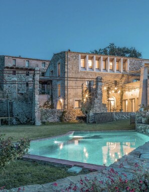Un bâtiment en pierre doté d’une piscine, entouré d’un mur de pierre et de verdure.