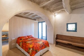 Une chambre à coucher avec un lit, un banc, une porte en arc de cercle et une fenêtre.