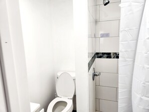 Un baño con inodoro, ducha y pared de azulejos.