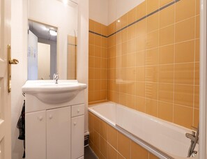Ein Badezimmer mit einem weißen Waschbecken, einem Spiegel und einer Badewanne mit orangefarbenen Fliesen.