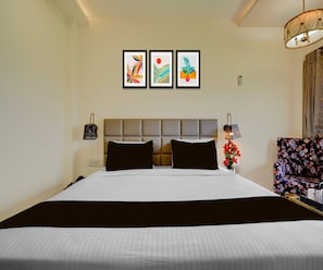 A hotel room with a large bed, a headboard, a nightstand, a lamp, and three framed artworks on the wall. - Suite Room Amar Resorrt (Motihari)