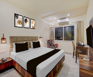 Una habitación de hotel con cama, escritorio, silla, televisor y obras de arte en la pared.