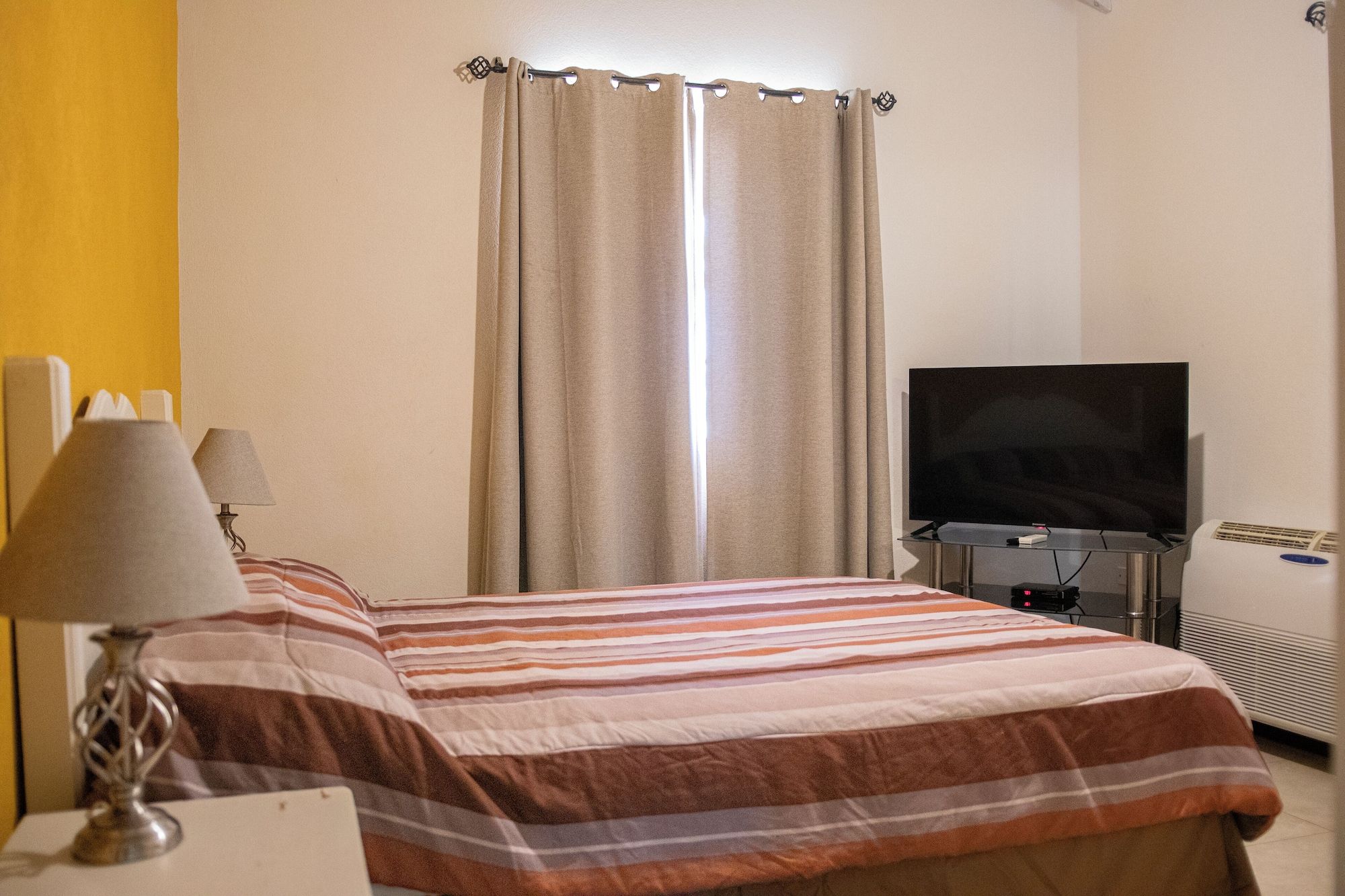 A hotel room with a bed, a television, a desk with a lamp, and a window with curtains.