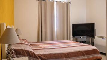 A hotel room with a bed, a television, a desk with a lamp, and a window with curtains.