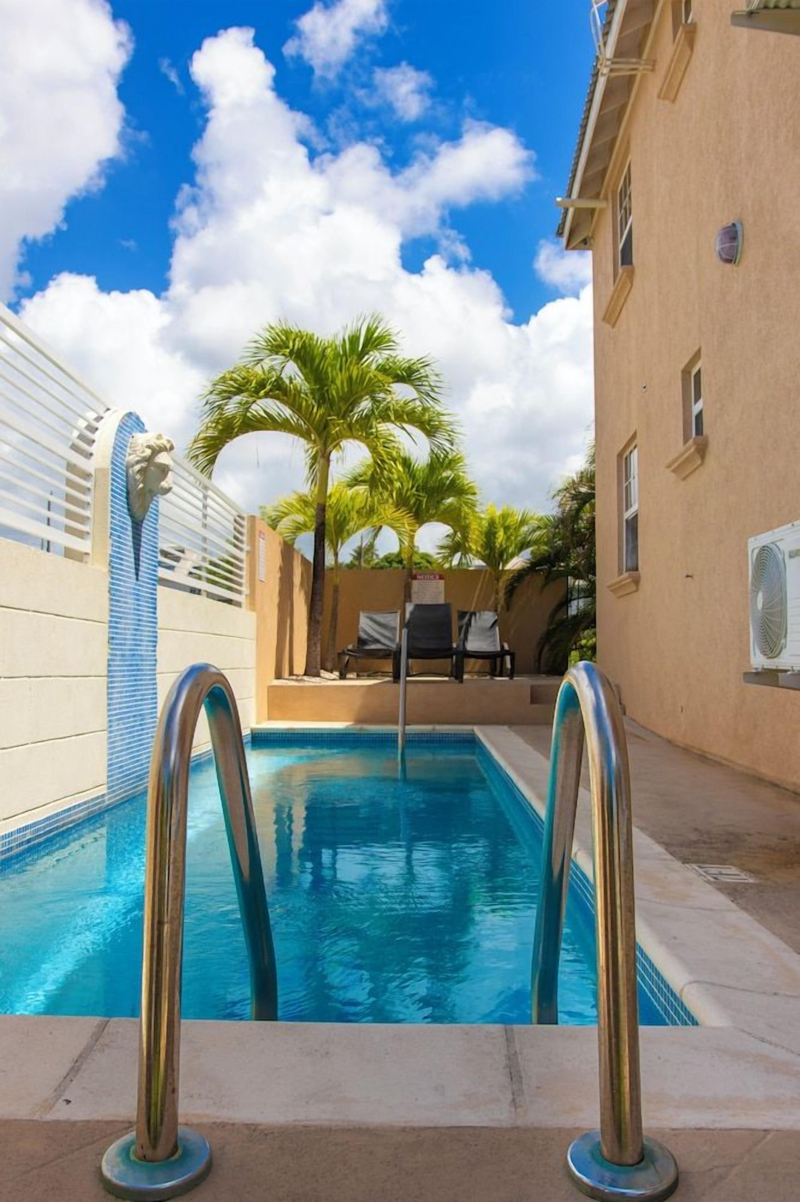 A swimming pool with metal railings, palm trees, and a clear blue sky.