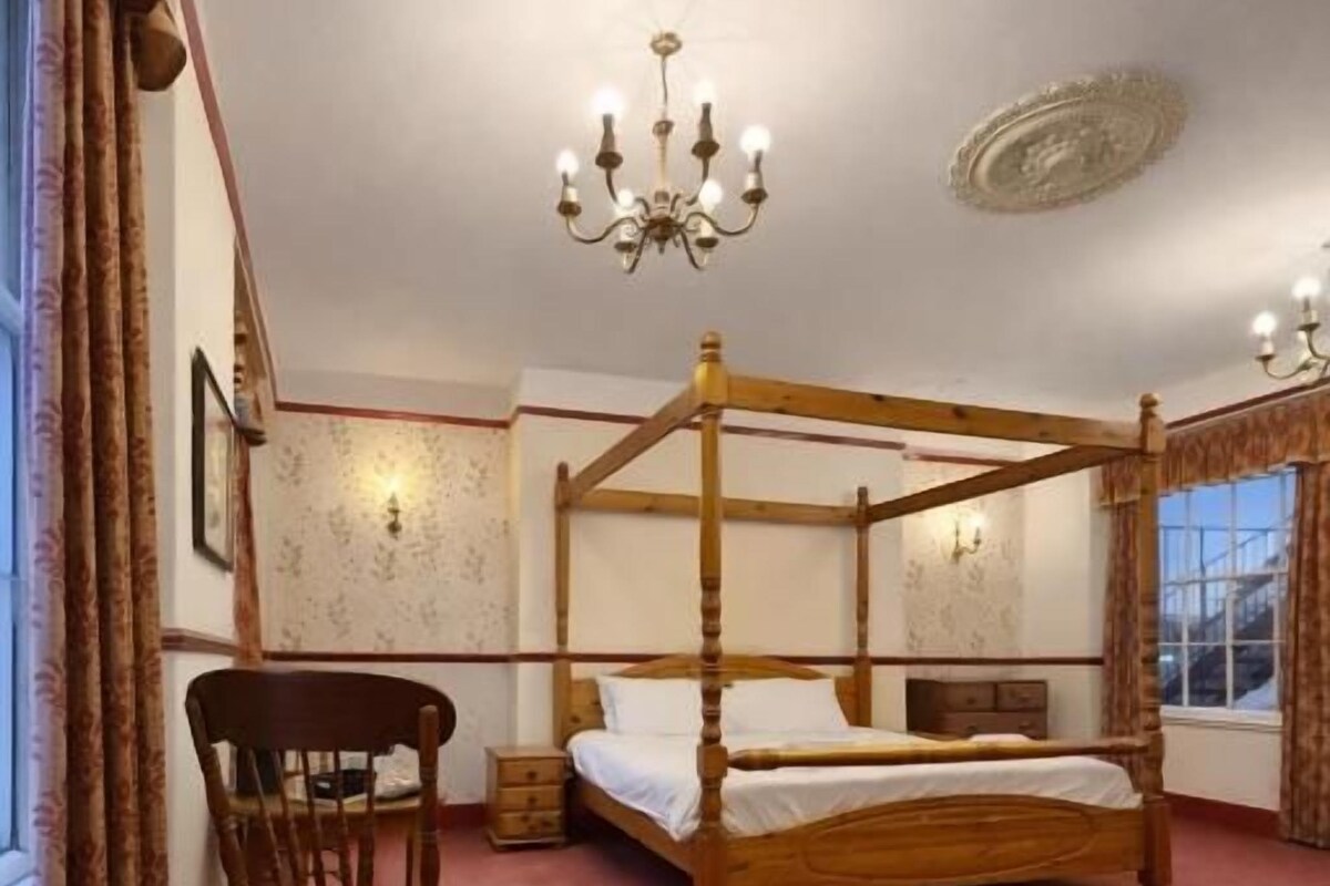 A four-poster bed in a room with a red carpet, a wooden chair, and a chandelier.