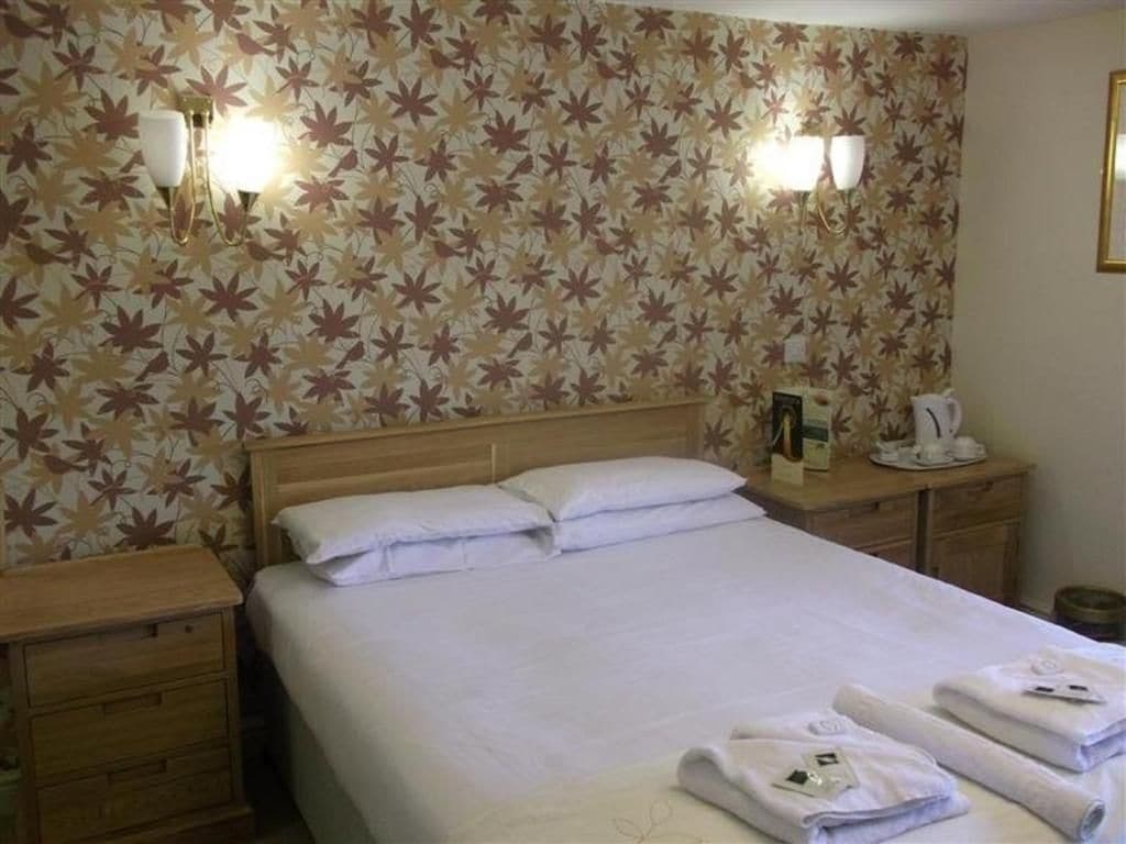 Une chambre d’hôtel comprenant un lit, deux tables de chevet, une petite table et une lampe fixée au mur.