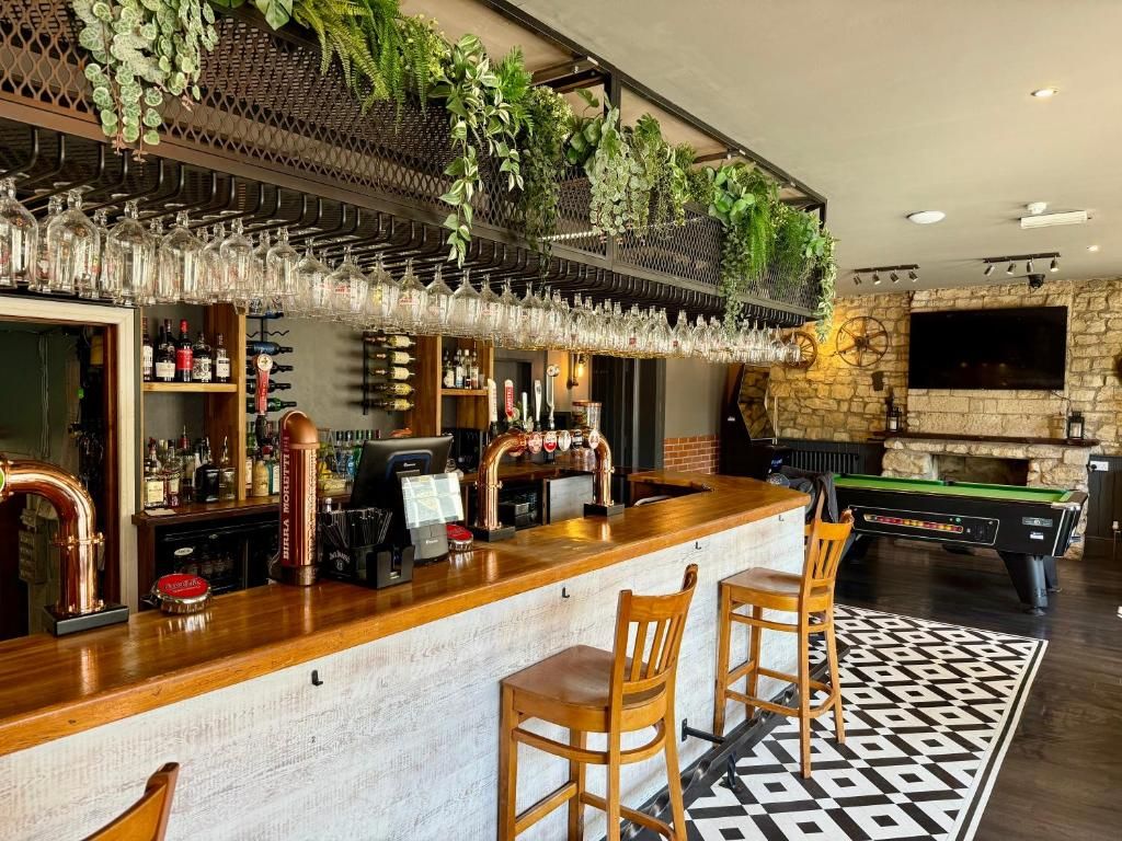 Zona de bar con mostrador de madera, taburetes, mesa de billar y televisor montado en una pared de piedra.