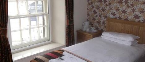 A hotel room with a bed, a window, a nightstand, and a wall with a leaf pattern.