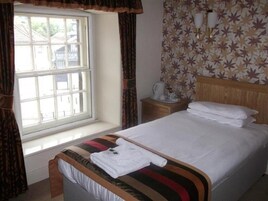Una habitación de hotel con cama, ventana, mesita de noche y pared con diseño de hojas.