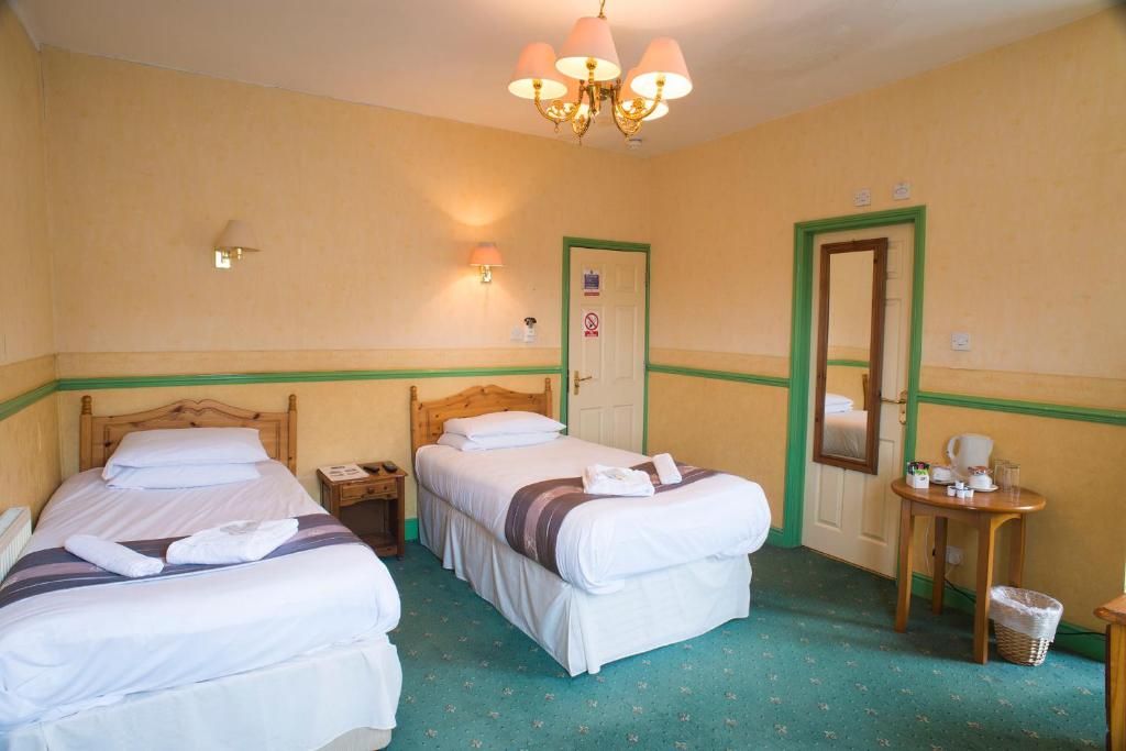 A hotel room with two beds, a wooden headboard, a small table with a chair, a mirror, and a chandelier.
