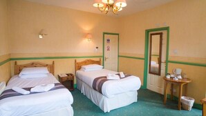 Ein Hotelzimmer mit zwei Betten, einem hölzernen Kopfteil, einem kleinen Tisch mit Stuhl, einem Spiegel und einer Chandelier.