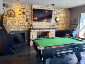 A billiards table in a room with stone walls, a mounted television, and a fireplace.