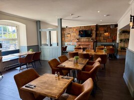 Un restaurante con mesas y sillas de madera, una pared de ladrillo con un televisor y una chimenea.