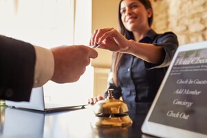 Mostrador de recepción de un hotel con pantalla digital mostrando opciones como 'Registro de Huéspedes' y 'Agregar Miembro al Servicio de Concierge'.