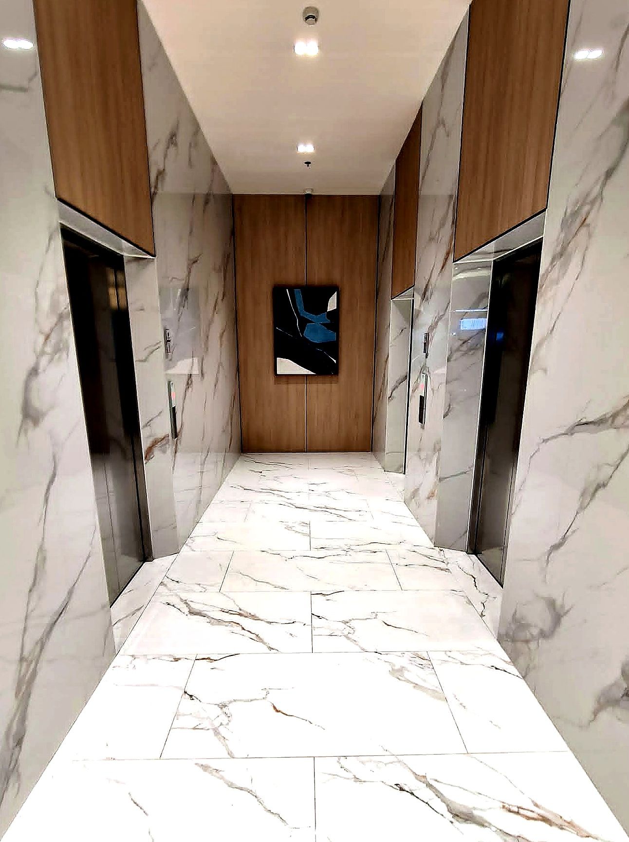 A corridor with marble flooring, wooden paneling, and a central wall-mounted artwork.