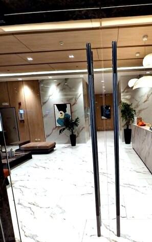 Un vestíbulo moderno con piso de mármol, una recepción, una zona de estar y un cuadro grande en la pared.