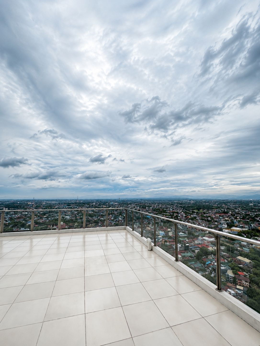Une terrasse sur le toit offrant une vue panoramique sur la ville, avec un sol carrelé et une rambarde en métal.