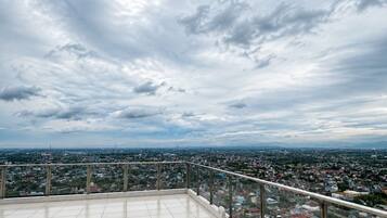 Une terrasse sur le toit offrant une vue panoramique sur la ville, avec un sol carrelé et une rambarde en métal.