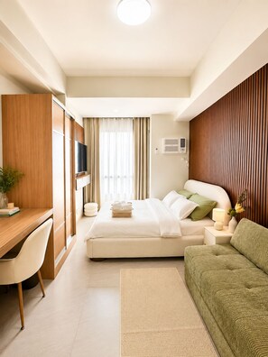 Habitación de hotel con cama, escritorio, silla, televisor y mesita de noche con lámpara y flores.