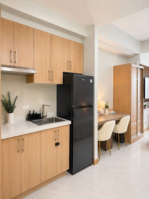 A modern kitchen with wooden cabinets, a black refrigerator, a sink, and a dining area with chairs.