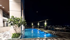 A rooftop pool area with lounge chairs and a view of the city at night. - Cozy studio in lovely Quezon City with refreshing AC (Quezon City)