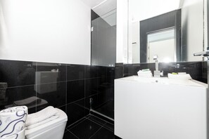 A modern bathroom with a white sink, black tiled walls, and a glass shower enclosure. - Luxury Miami Beach Apartments By Michigan (Miami Beach)