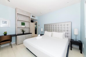 A hotel room with a large bed, a desk, a chair, and a small kitchenette. - Luxury Miami Beach Apartments By Michigan (Miami Beach)