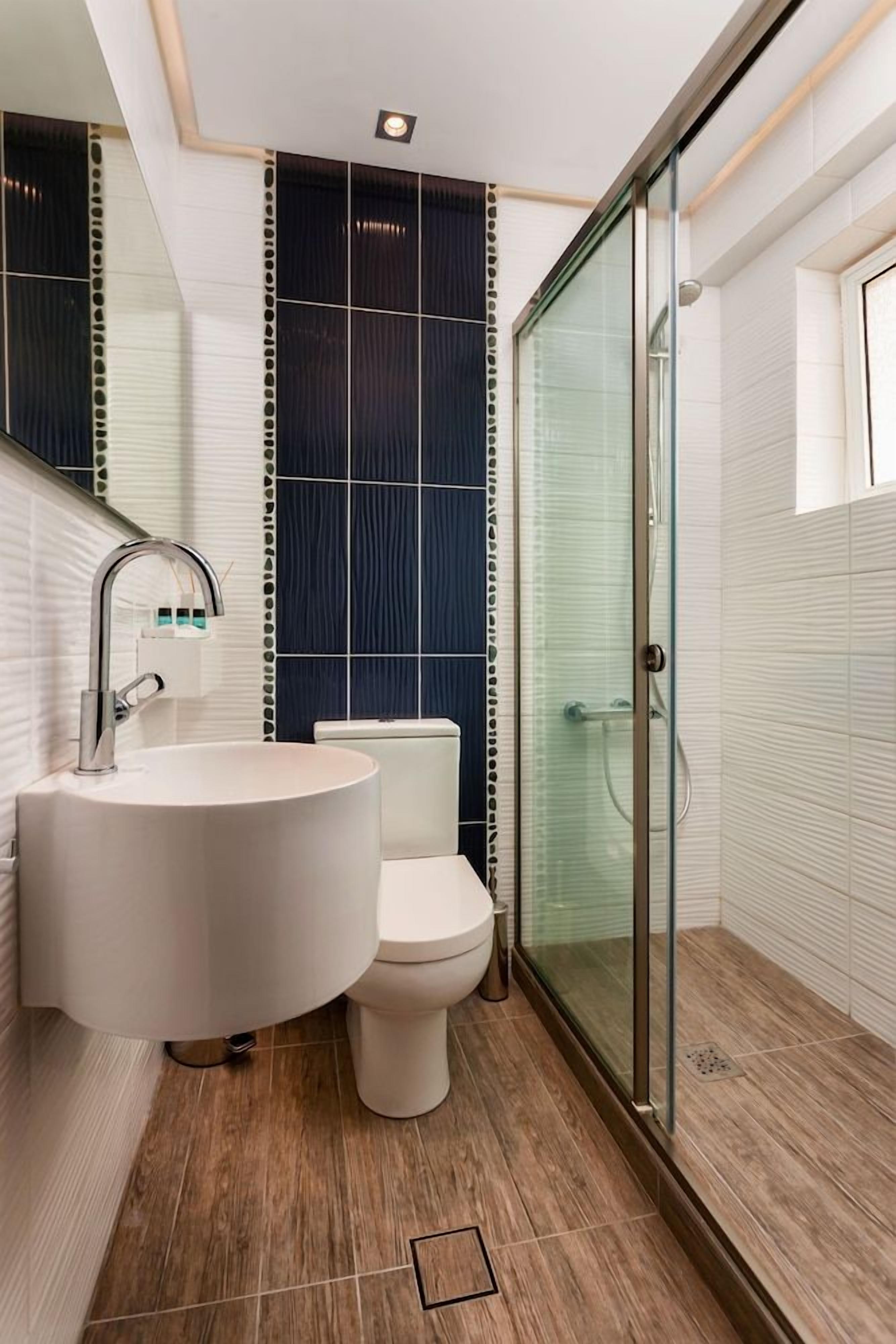 Een moderne badkamer met een rond wastafel, toilet en een douche met glazen wanden.