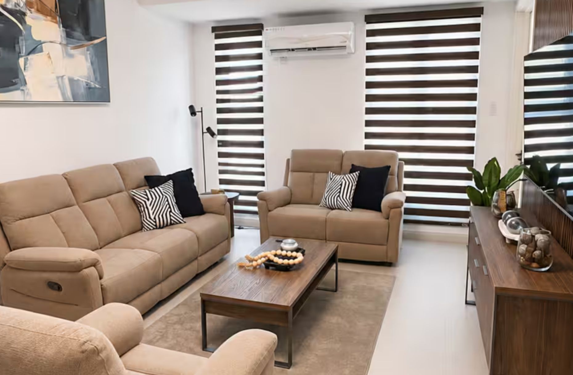 Una sala de estar con un sofá color beige, un sofá más pequeño, una mesa de centro y una mesita auxiliar con objetos decorativos.
