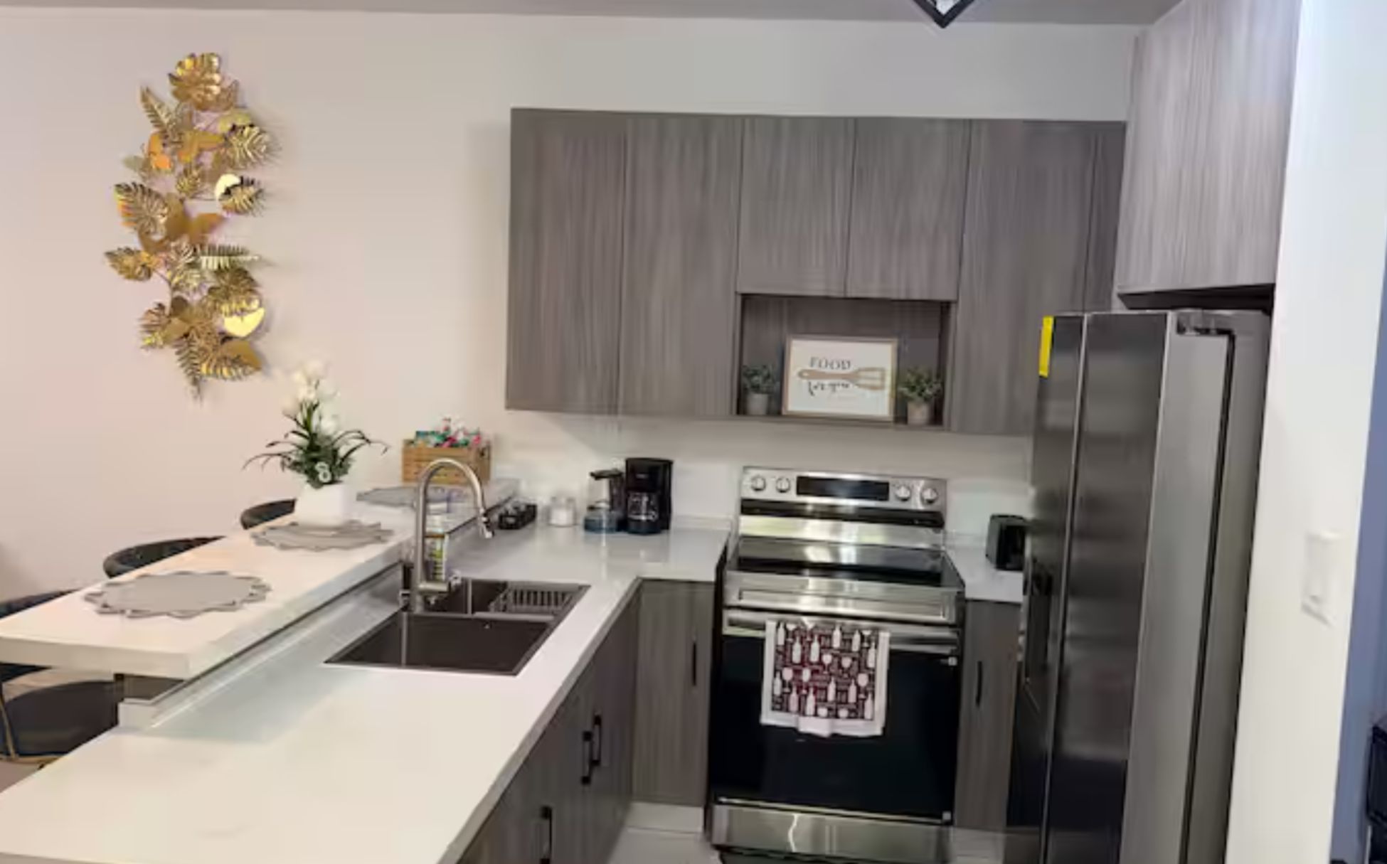 Una cocina moderna con electrodomésticos de acero inoxidable, encimera blanca y un elemento decorativo en la pared.