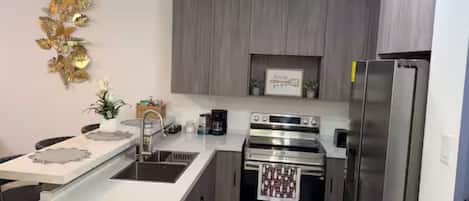 A modern kitchen with stainless steel appliances, a white countertop, and a decorative wall piece.