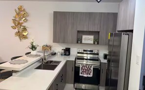 Une cuisine moderne dotée d’appareils électroménagers en acier inoxydable, d ’un plan de travail blanc et d’un élément décoratif mural.